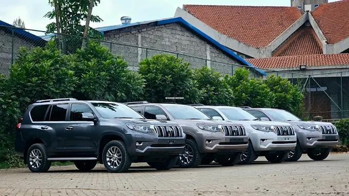 A beige Toyota Land Cruiser safari vehicle parked at the terminal building drop-off zone, showcasing an official car rental with driver Kigali package from Self Drive Rwanda