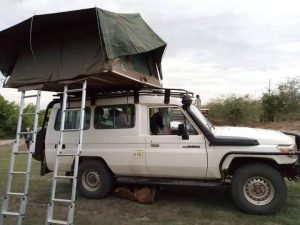 Overland safari vehicle with dual rooftop tents deployed at a scenic wilderness campsite during sunset in Rwanda